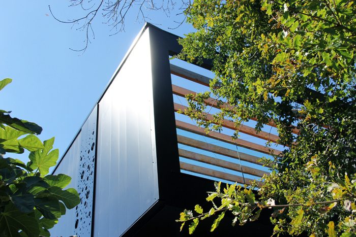 Surélévation Maison F. — Le bardage perforé dans la végétation